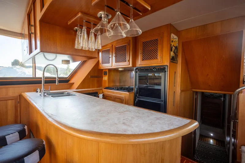 Mbellish Yacht Photos Pics 1988 Symbol 51 Motoryacht kitchen with wooden cabinetry, marble countertop, and hanging glassware.