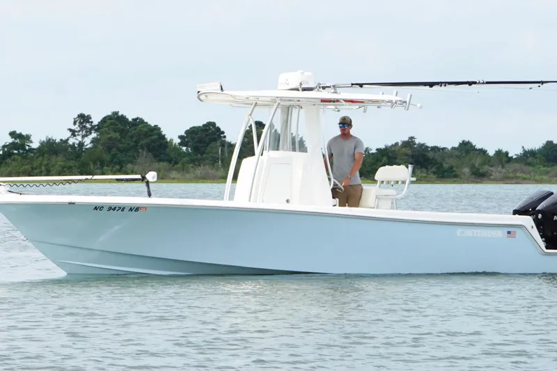  Yacht Photos Pics 2024 Contender 25 Tournament boat on water, with person steering, trees in background.