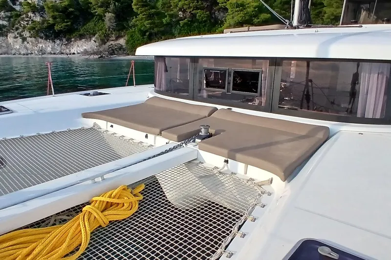 Stolos Yacht Photos Pics 2020 Lagoon 42 catamaran deck with netting and sunbathing area, anchored near a forested shoreline.