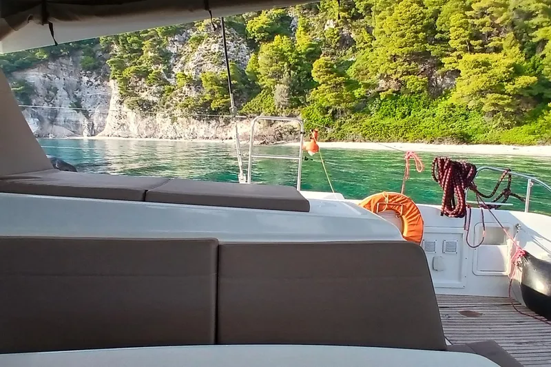 Stolos Yacht Photos Pics Lagoon 42 catamaran, 2020 model, anchored near scenic rocky coastline with lush greenery.