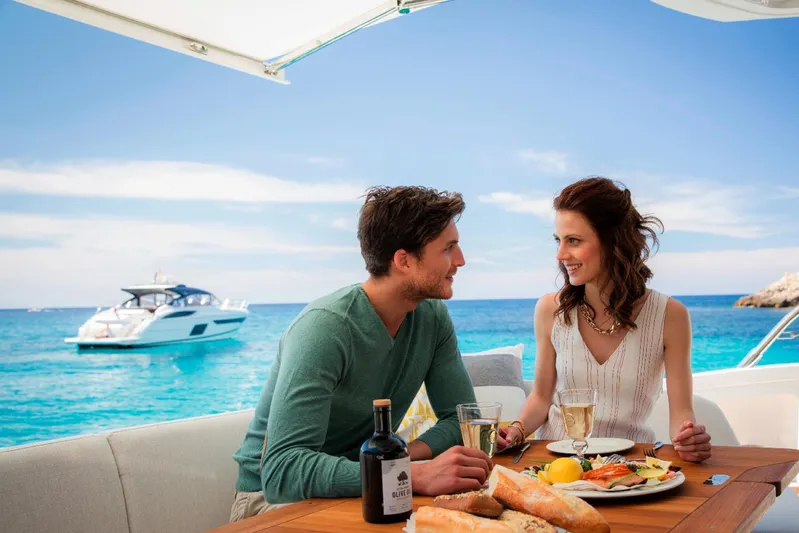  Yacht Photos Pics Couple dining on a yacht with 2018 Princess S65 in the background, enjoying a sunny day.