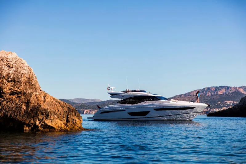  Yacht Photos Pics 2018 Princess S65 yacht cruising near rocky coastline under clear blue sky.