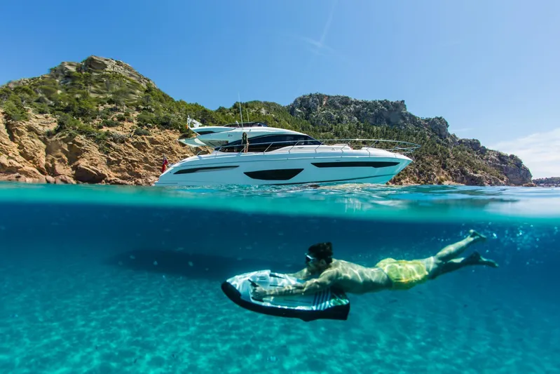  Yacht Photos Pics Man snorkeling near 2018 Princess S65 yacht in clear blue water by rocky coastline.