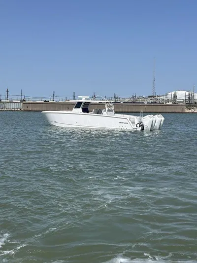  Yacht Photos Pics 2024 Twin Vee 400 GFX boat cruising on a calm waterway near an industrial shoreline.