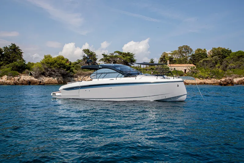  Yacht Photos Pics 2026 Beneteau Gran Turismo 40 yacht cruising on clear blue water near a rocky shoreline.