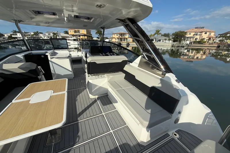  Yacht Photos Pics 2021 Aquila 32 Sport boat interior with seating and table, docked by waterfront homes.