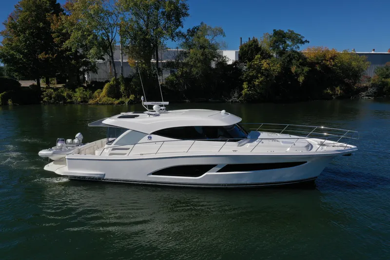  Yacht Photos Pics 2025 Riviera 465 SUV yacht cruising on a serene river under a clear blue sky.