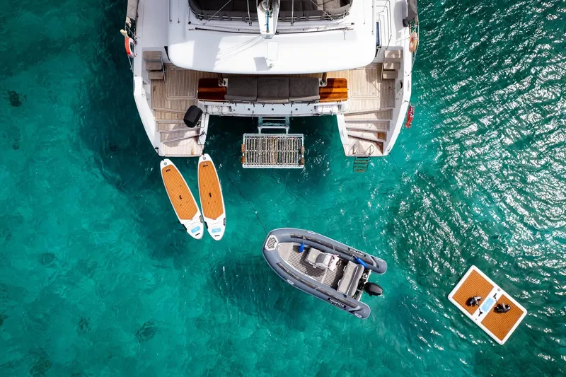 Bluewinds Yacht Photos Pics Aerial view of Lagoon 560 S2 yacht with paddleboards and dinghy in turquoise water.