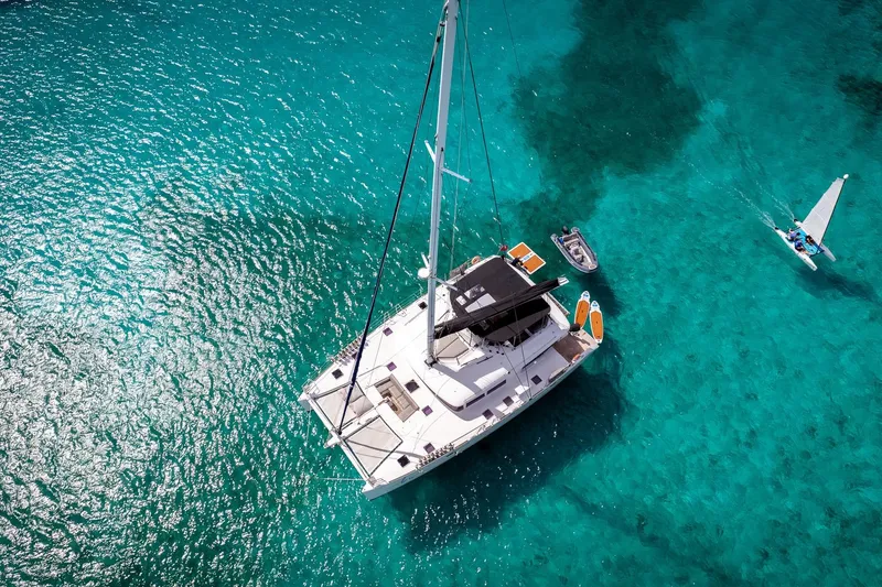 Bluewinds Yacht Photos Pics Aerial view of 2023 Lagoon 560 S2 catamaran on clear turquoise water.