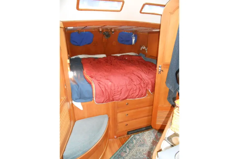 Second Kiss Yacht Photos Pics Cozy cabin interior of 1989 Norseman 447 sailboat with wooden furnishings and red bedding.