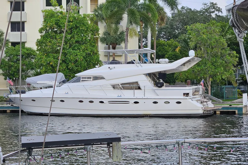 "fortunate" Yacht Photos Pics 1995 JOHNSON 65 Flybridge Motoryacht docked by lush greenery and waterfront buildings.