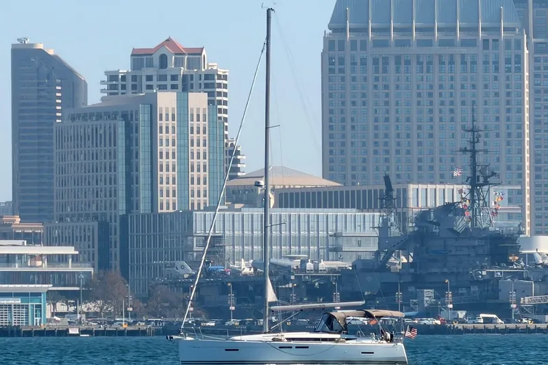 Jenni Yacht Photos Pics 2015 Jeanneau Sun Odyssey 409 sailing near urban skyline and naval ship.