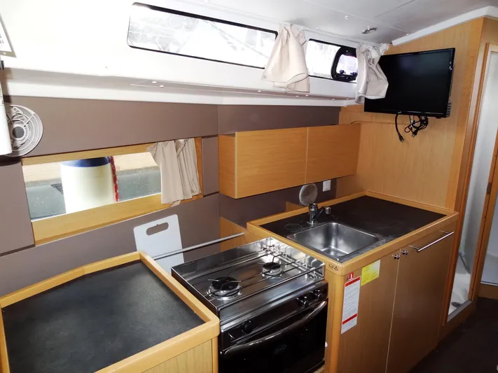 America Yacht Photos Pics Modern kitchen area in 2018 Beneteau Oceanis 38 sailboat with stove, sink, and TV.