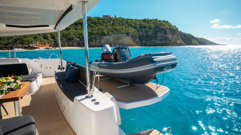 Infinity Yacht Photos Pics 2023 Lagoon 46 yacht with tender, anchored in scenic blue waters near a lush coastline.