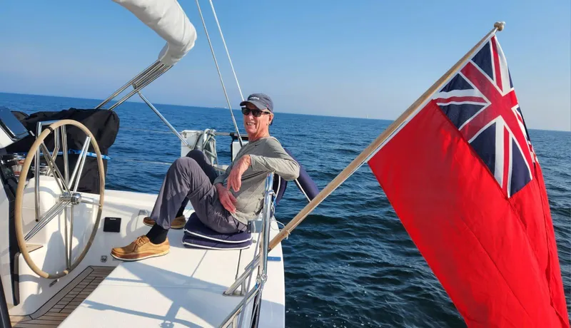 Yula Yacht Photos Pics Man relaxing on 2024 X-Yachts Xc 47 sailboat with red ensign flag.