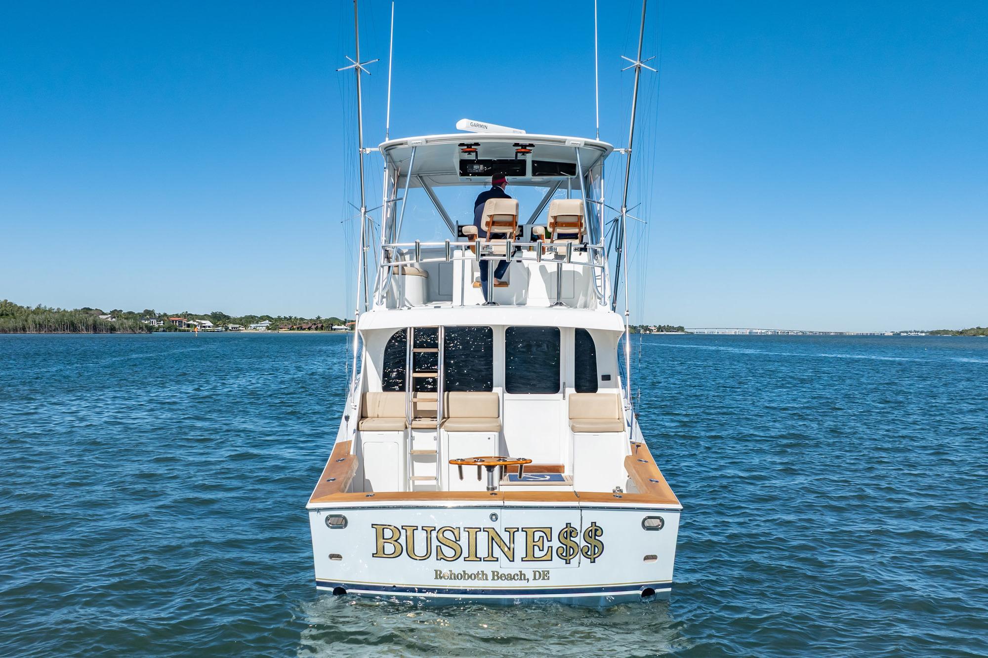 Luxury yacht "BUSINE$$" on water, Rehoboth Beach, DE, clear blue sky.