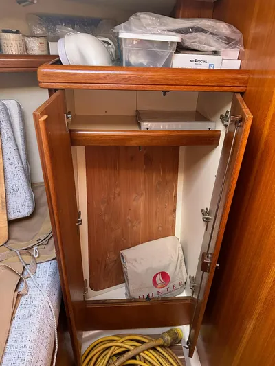 Yacht Photos Pics Empty wooden cabinet inside a 2005 Hunter 38 sailboat, with storage items and a coiled hose.
