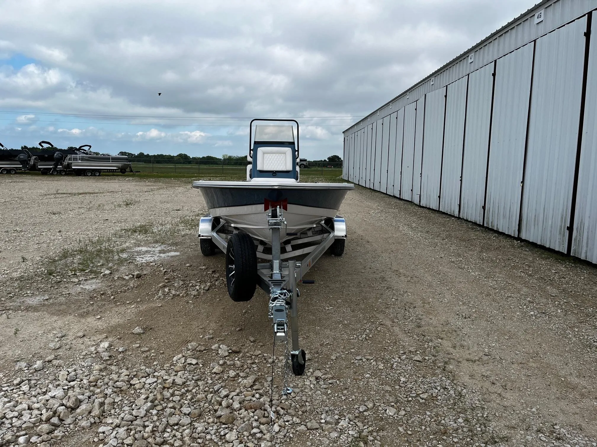 2025 Blazer Bay 2220 Fisherman boat on trailer, parked on gravel near a large building.