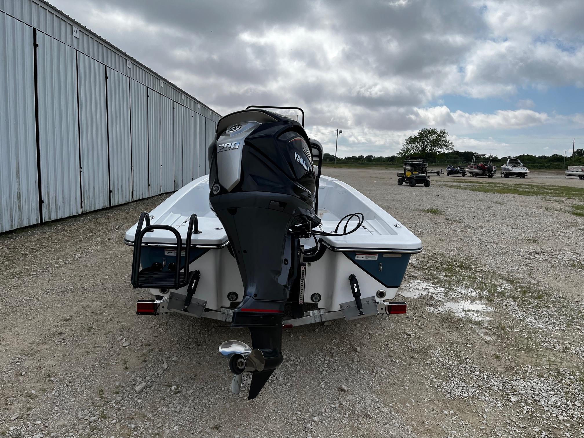 2025 Blazer Bay 2220 Fisherman boat with outboard motor, parked on gravel near a metal building.