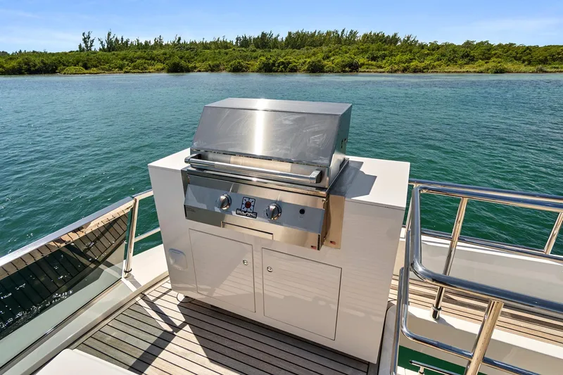 Smile Yacht Photos Pics Outdoor grill on 2023 Astondoa 66 Flybridge yacht, overlooking serene water and lush greenery.