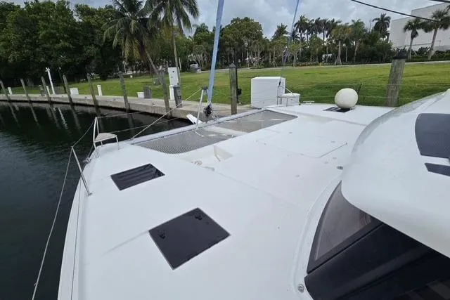 Island Nomad Yacht Photos Pics 2022 Fountaine Pajot Tanna 47 catamaran docked near lush greenery and calm waters.