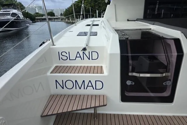 Island Nomad Yacht Photos Pics 2022 Fountaine Pajot Tanna 47 yacht with "Island Nomad" on steps, docked by water.