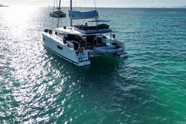 Island Nomad Yacht Photos Pics 2023 Fountaine Pajot Tanna 47 catamaran sailing on clear turquoise waters.