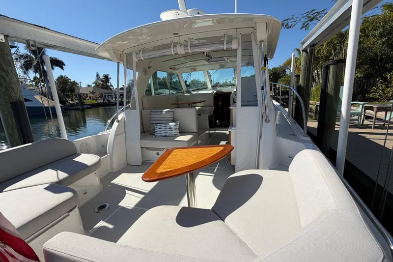 Pivot Yacht Photos Pics 2023 Back Cove 340 boat interior with seating and wooden table, docked by a scenic waterfront.