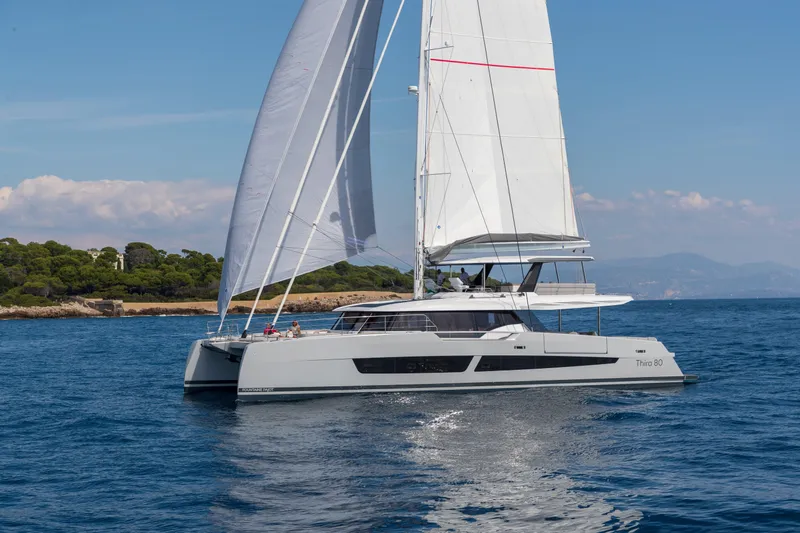 Serenissima III Yacht Photos Pics 2025 Fountaine Pajot Thira 80 sailing on calm blue waters near a scenic coastline.